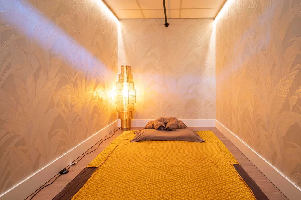 Behandelkamer met massagemat op de vloer en een gouden lamp